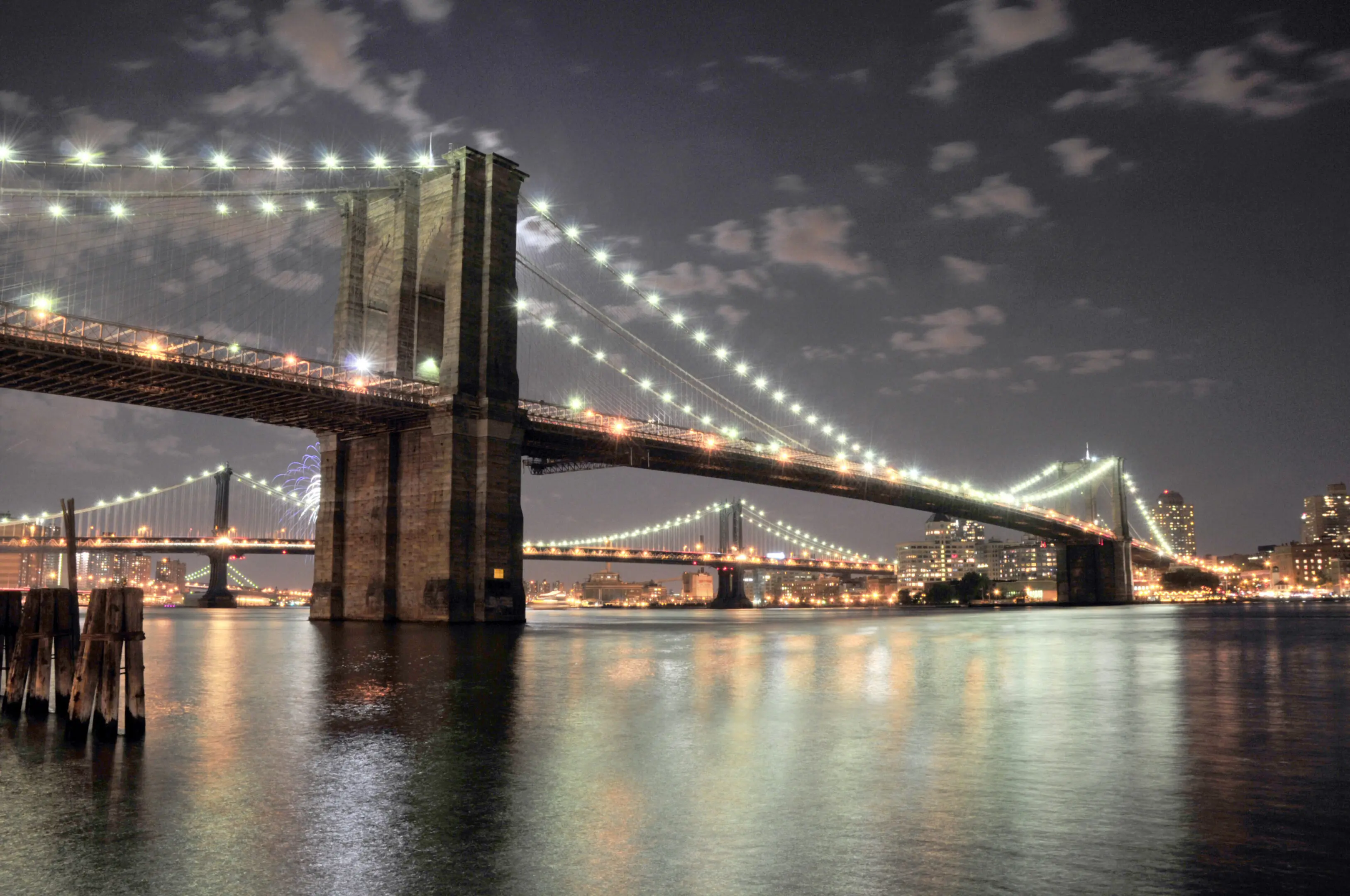 Night view of an illuminated suspension bridge over calm water.