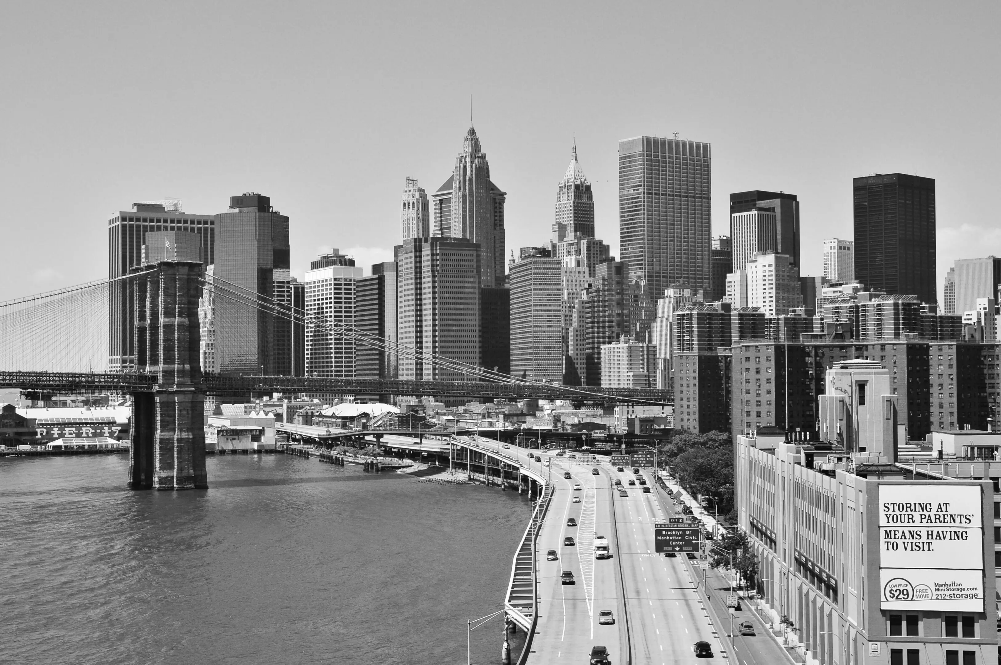 Black and white cityscape with skyscrapers and highway by the water.